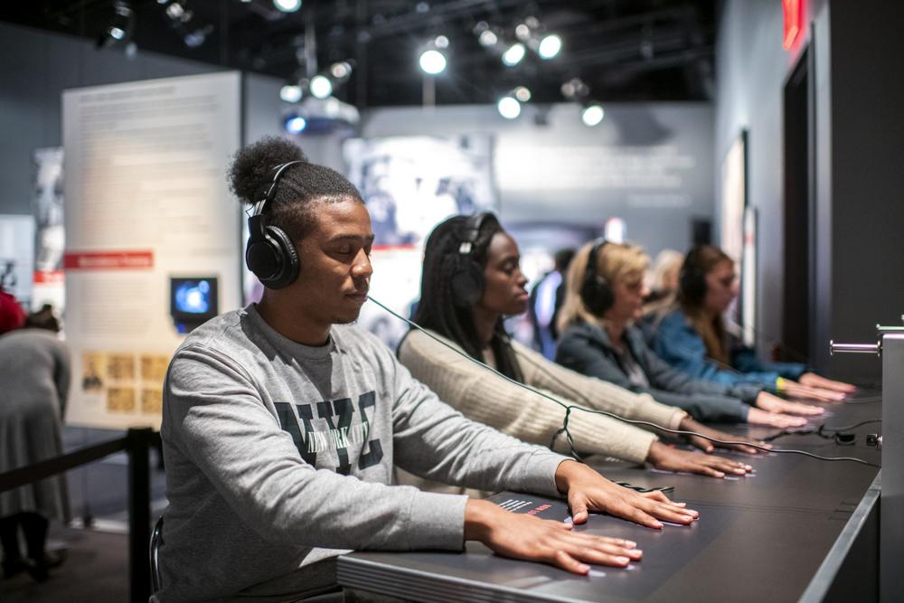 Visitors of the Center for Civil and Human Rights in Atlanta sit at a lunch counter with a pair of headphones and listen to a dramatic reenactment of the Woolworth's sit-in. 