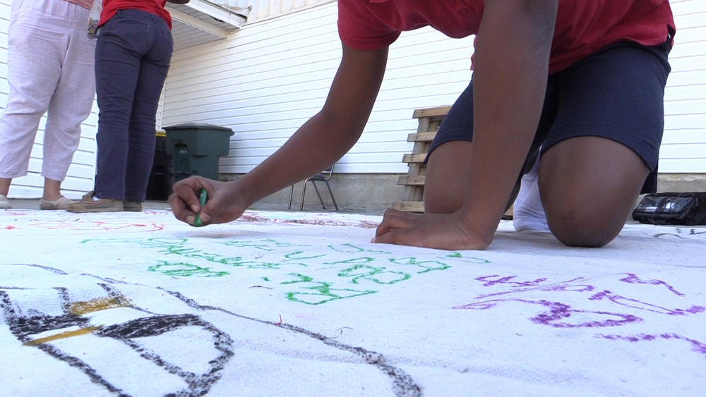 Student draws on peace mural, to go up in her neighborhood. 