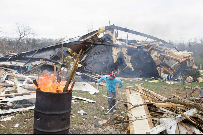 A boy burns scraps of wood from a destroyed home in a barrel fire. Temperatures stayed in the 40s in the area following Sunday's storms.