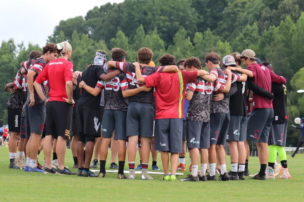 The U-20 team huddles at a tournament while Coach T.J. Martin talks with them.