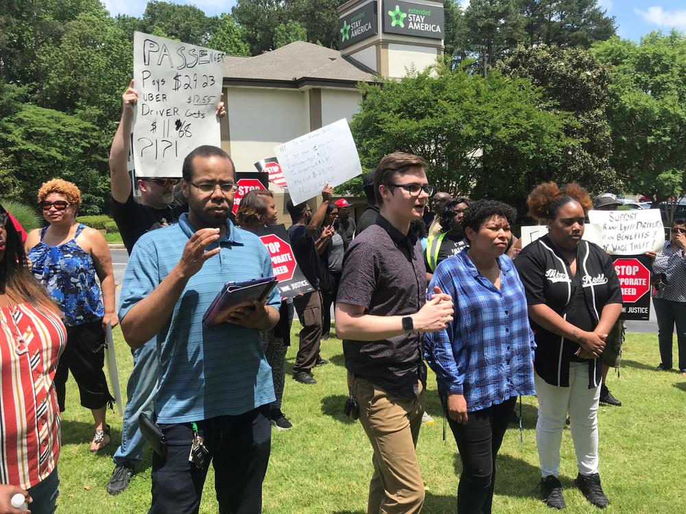 Austin Gates, with Rideshare Drivers United Georgia, is flanked by Uber drivers demanding better benefits and safety improvements. 