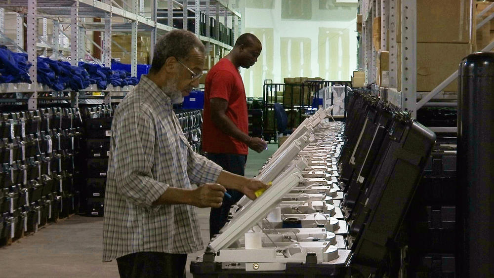 This Sept. 22, 2016 file photo shows employees of the Fulton County Election Preparation Center in Atlanta test electronic voting machines. A security researcher disclosed a gaping security hole at the outfit that manages Georgia's elections.