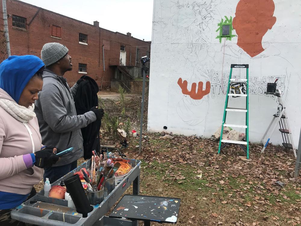 Yungai and his wife prepare paint as he continues to paint his mural.