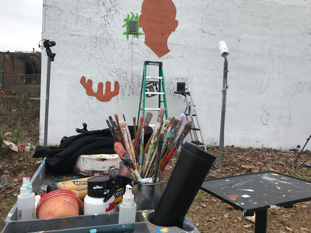 Yungai's paintbrushes sit in front of the wall where he paints his mural.