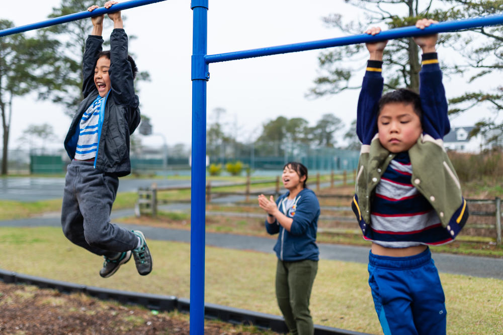 Thu Pham, center, encourages Henry, left, and Hayle, as they climb pull-up bars at a park on Chinqoteague Island, Md., on April 14, 2019.