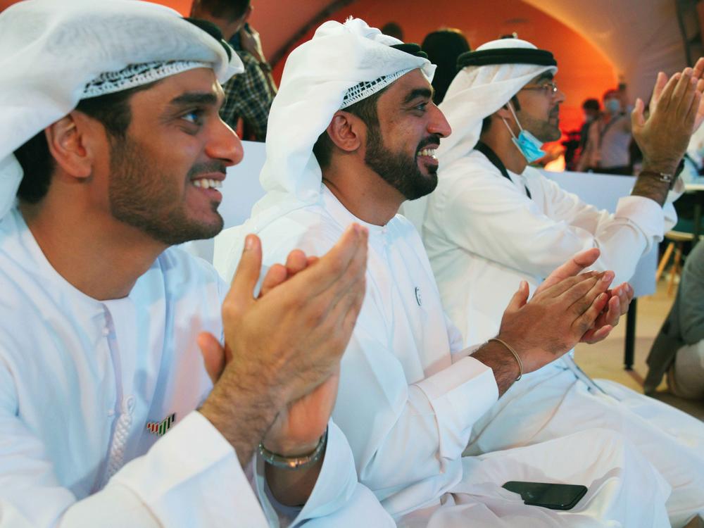 Emirati men clap as they watch the launch of the 