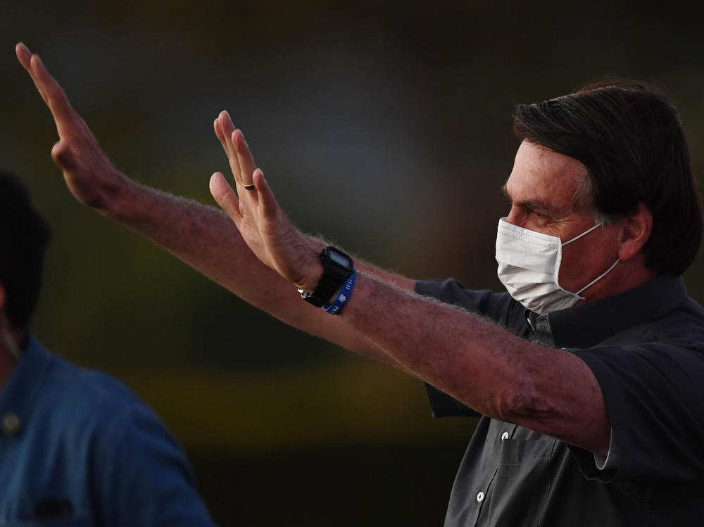 Brazilian President Jair Bolsonaro waves to supporters from the Alvorada Palace in Brasilia on Monday, the same day that two more of his Cabinet ministers were diagnosed with COVID-19.