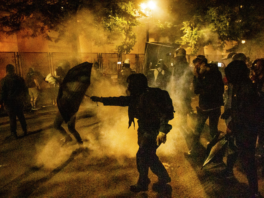 Protesters walk through chemical irritants deployed by federal agents in Portland, Ore. The Justice Department inspector general says he is investigating federal officers' roles in responding to protests in Portland and Washington, D.C.