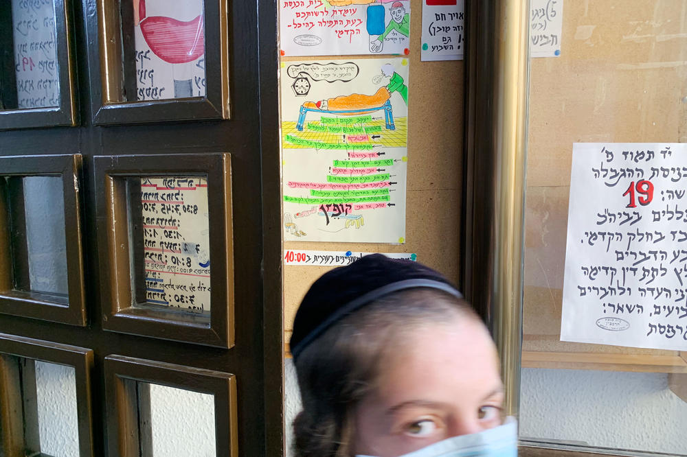 A young worshiper passes the signs and cartoons Yehezkel Cahn has tacked up at the entrance to the small synagogue. The number 19 in red (at right) indicates the maximum number of worshipers allowed indoors, per Israeli government guidelines at the time.