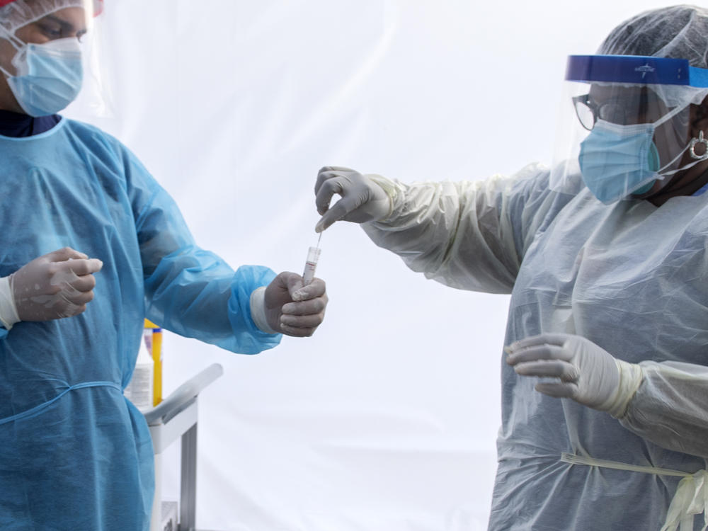A health worker puts a nasal swab sample into a tube in a tent at a COVID-19 testing site at St. John's Well Child and Family Center in Los Angeles.
