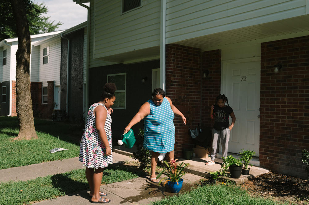 Talayla Feggins (left) and Tranese Feggins (right) help their mother, Harriet Feggins, water flowers at their home in west Atlanta. Harriet has shut off the power in some rooms and has hung blackout curtains to try to keep the house cool and her electric bill low.
