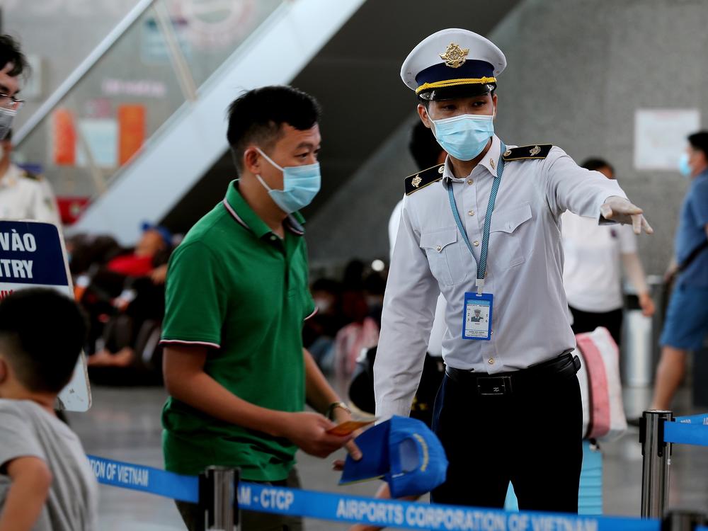 A staff member from Vietnam's disease control authority assists passengers as they queue up for temperature checks at the departure terminal at Da Nang's international airport on Monday.