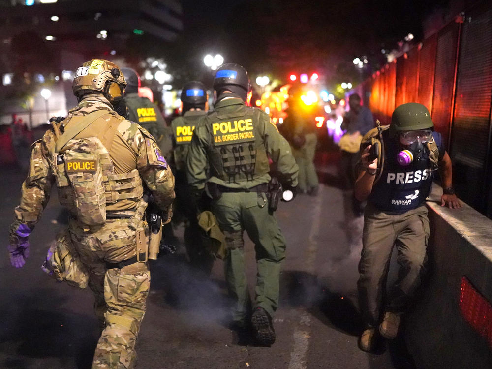 A journalist runs past federal officers during a protest against racial injustice in front of the Mark O. Hatfield U.S. Courthouse on July 30 in Portland, Ore.