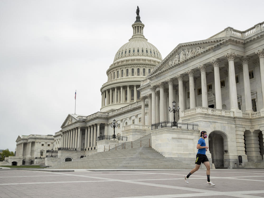 A man with a mask depicting American flags jogs past the U.S. Capitol in April. More than three-quarters of respondents to the NPR/Ipsos poll support enacting state laws to require mask wearing in public at all times.