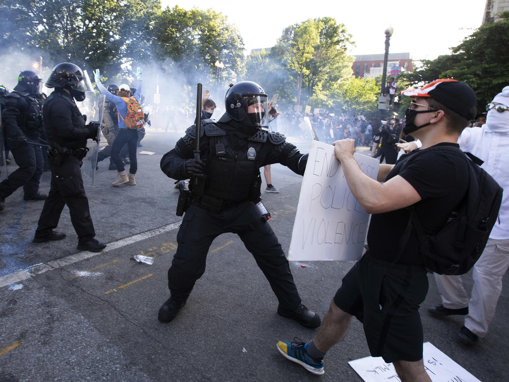 A law enforcement officer raises a baton and tear gas is fired during protests near the White House on June 1.