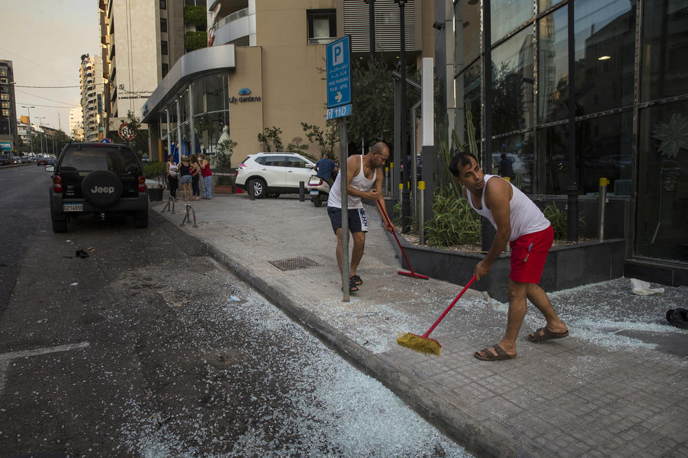 Residents sweep glass off the sidewalk after the large explosion in Beirut. Images from the scene show that entire blocks of buildings were wrecked along the port, their structural supports crumpled by the blast. Numerous fires broke out, sending black smoke into the sky.