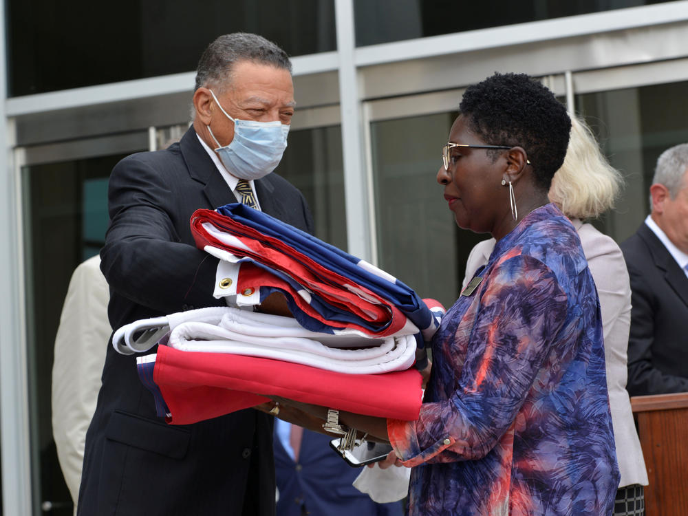 Reuben Anderson (left), former Mississippi Supreme Court justice, hands the Mississippi state flag to Pamela Junior, director of the Two Mississippi Museums, in Jackson, Miss., on July 1, after a bill was signed into law that would replace the state flag that includes a Confederate emblem.