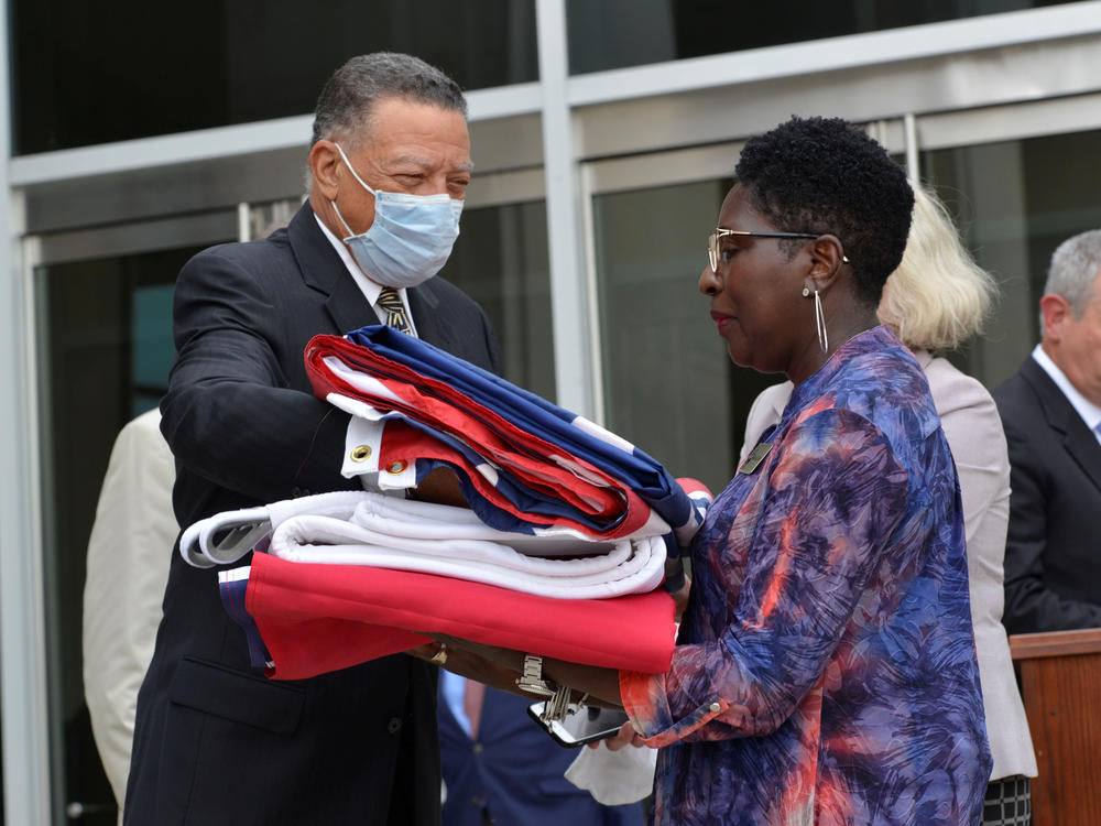 Reuben Anderson (left), former Mississippi Supreme Court justice, hands the Mississippi state flag to Pamela Junior, director of the Two Mississippi Museums, in Jackson, Miss., on July 1, after a bill was signed into law that would replace the state flag that includes a Confederate emblem.