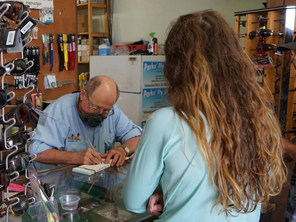 Richard Parks fills out a fishing license for a customer at his shop in Gardiner, Mont. After a slow start to the summer tourism season, he says, business is now booming.