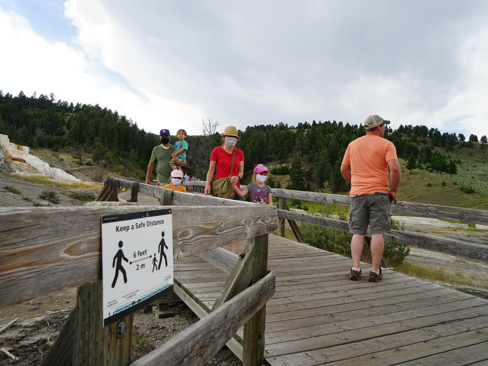 Signs urge people to stay 6 feet apart on a walkway at Yellowstone National Park's Mammoth Hot Springs. But it's difficult to maintain distancing on narrow trails.