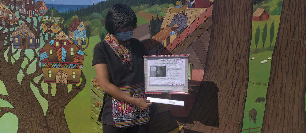 Greacen holds up one of the mask dispensers that she designed. They are made of recycled campaign signs.