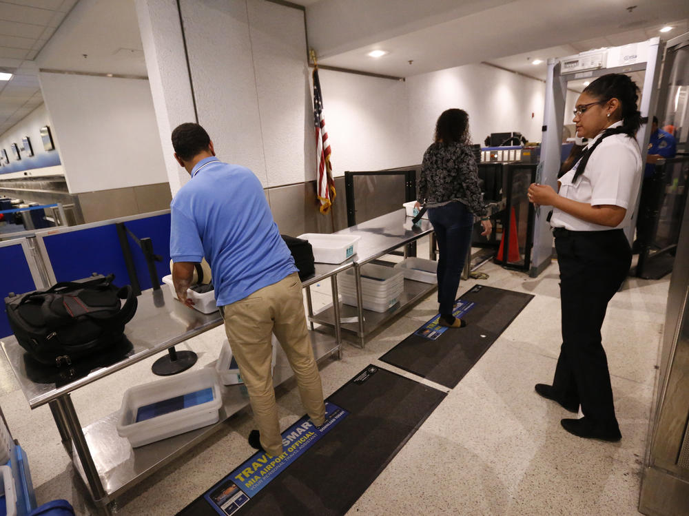A Transportation Security Administration officer watches as travelers put their items through an X-ray machine in 2017 at Miami International Airport. The TSA says it's finding significantly more firearms in carry-on luggage despite a huge drop in air travel.