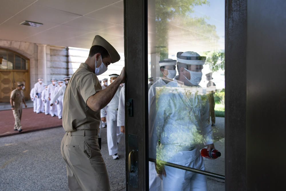A plebe summer detailer holds the door for a company of plebes as they enter a building on campus.