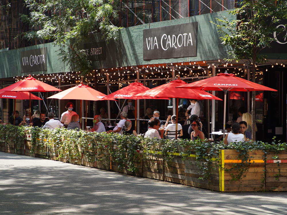 People dine under red umbrellas outside Via Carota restaurant in New York City's West Village. As the city continues to reopen, it is allowing restaurants to expand outdoors.
