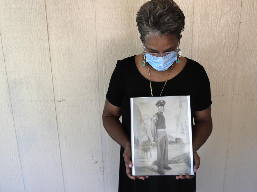 Belvin Jefferson White poses with a portrait of her father, Saymon Jefferson, who died from COVID-19, in Baton Rouge, La., in May.