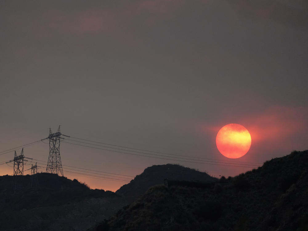 The sun sets through smoke created by the Ranch Fire on Aug. 13, 2020, in Azusa, Calif. A heat wave has prompted electrical providers to issue the first rolling blackouts in the state since 2001.