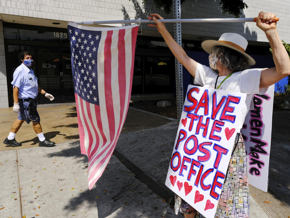 Erica Koesler of Los Angeles demonstrates outside a USPS post office as a postal worker walks by in the background on Saturday. The USPS has warned states coast to coast that it cannot guarantee all ballots cast by mail for the November election will arrive in time to be counted, even if mailed by state deadlines.