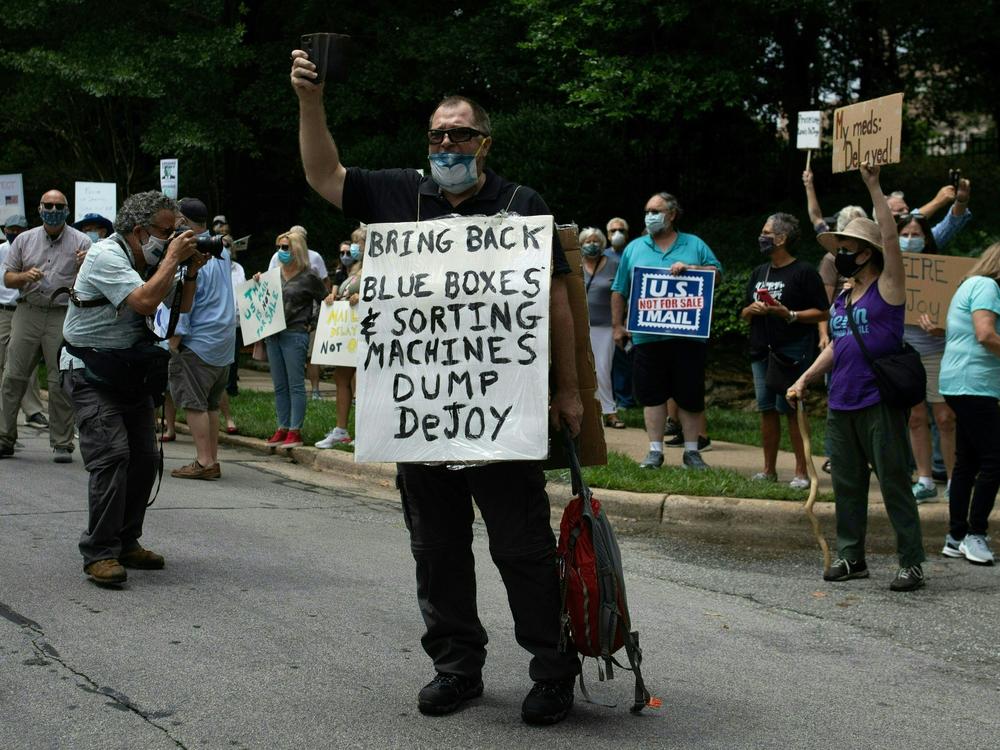 A group of protestors holds a demonstration in front of Postmaster General Louis DeJoy's home in Greensboro, N.C. on Sunday. DeJoy has recently come under fire for changes made at the U.S. Postal Service that have delayed mail in advance of the November elections.