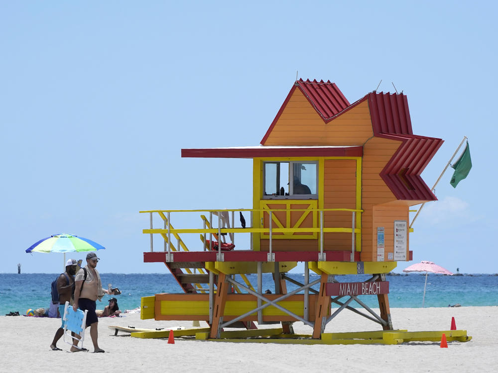 Beachgoers walk past a lifeguard tower on a nearly empty beach on Aug. 11 in Miami Beach, Fla.