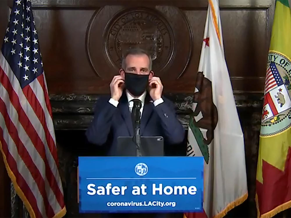 Los Angeles Mayor Eric Garcetti puts on a face mask during a news briefing in April.