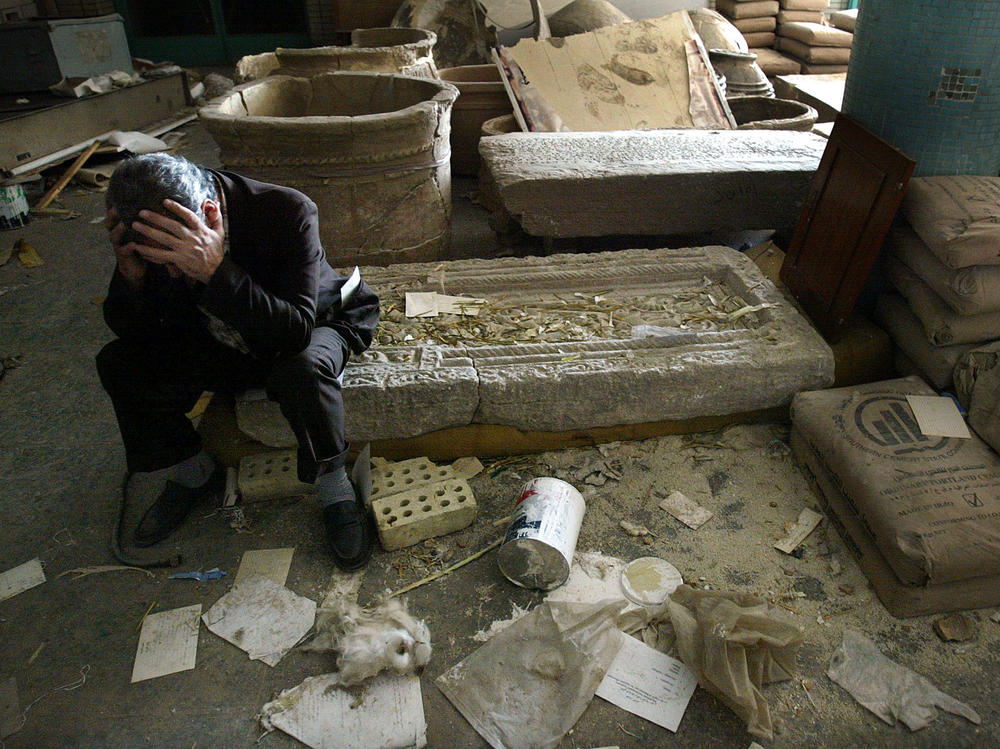 Iraqi National Museum Deputy Director Musin Hassan holds his head in his hands as he sits amid destroyed artifacts in the Baghdad museum in 2003.