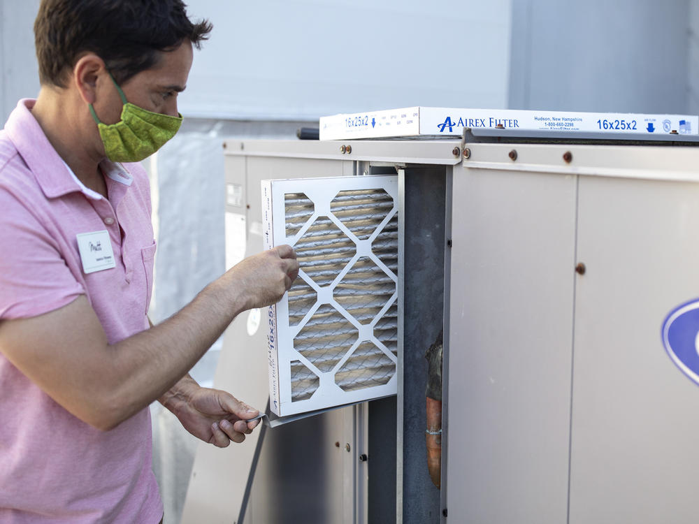 Mark Marston slides a MERV 13 air filter into the HVAC system outside Basics Fitness Center in Portland, Maine, on July 21. The gym bought these filters and made other changes to its ventilation, including bringing in more outside air, to help reduce the spread of the coronavirus.