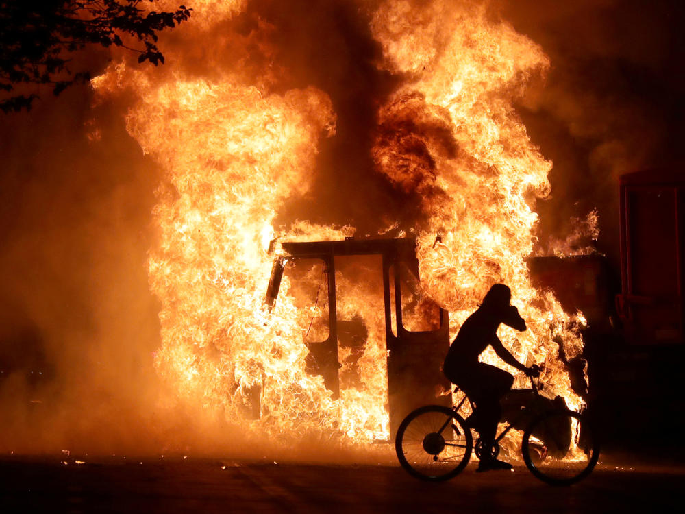 A man on a bike rides past a city truck on fire outside the Kenosha County Courthouse in Kenosha, Wis., during protests following the police shooting of Jacob Blake, a Black man, on Sunday.