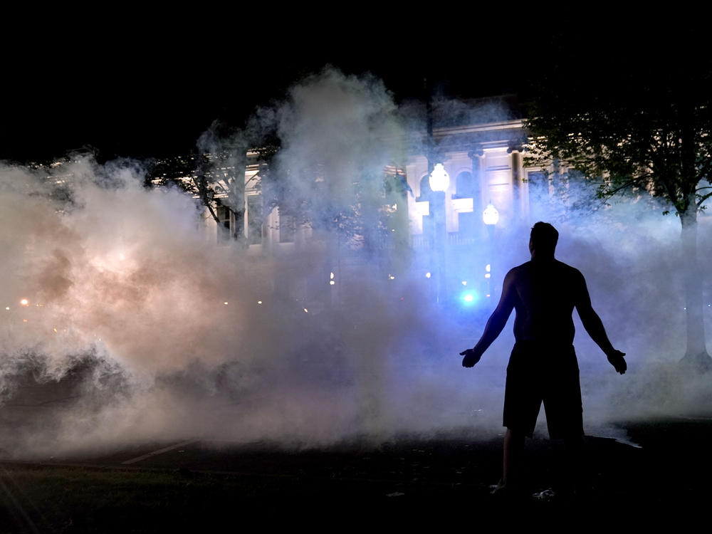A protester stands near a cloud of tear gas fired by police late Monday outside the Kenosha County Courthouse.