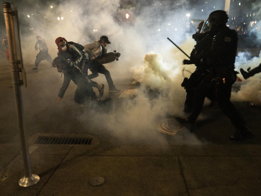 Protesters scramble to get away from approaching police firing tear gas and impact munitions to disperse protesters in downtown Portland during 4th of July demonstrations against systemic racism and police violence.
