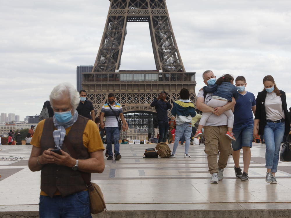 People wearing masks walk near the Eiffel Tower in Paris on Thursday, the same day that the government made masks mandatory in all the city's public outdoor spaces.