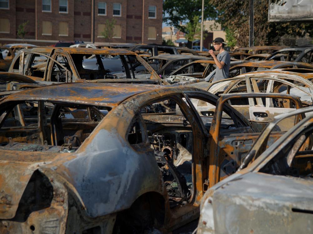 A young man walks through the lot of a Kenosha car dealership that was burned during Sunday night's protests over the police shooting of Jacob Blake.