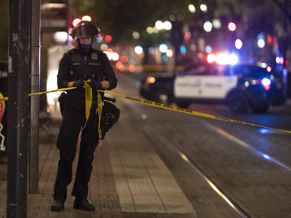 A Portland police officer ties a police line around the scene of a fatal shooting in Portland Saturday. It's the latest incident after weeks of Trump supporters clashing with counterprotesters.