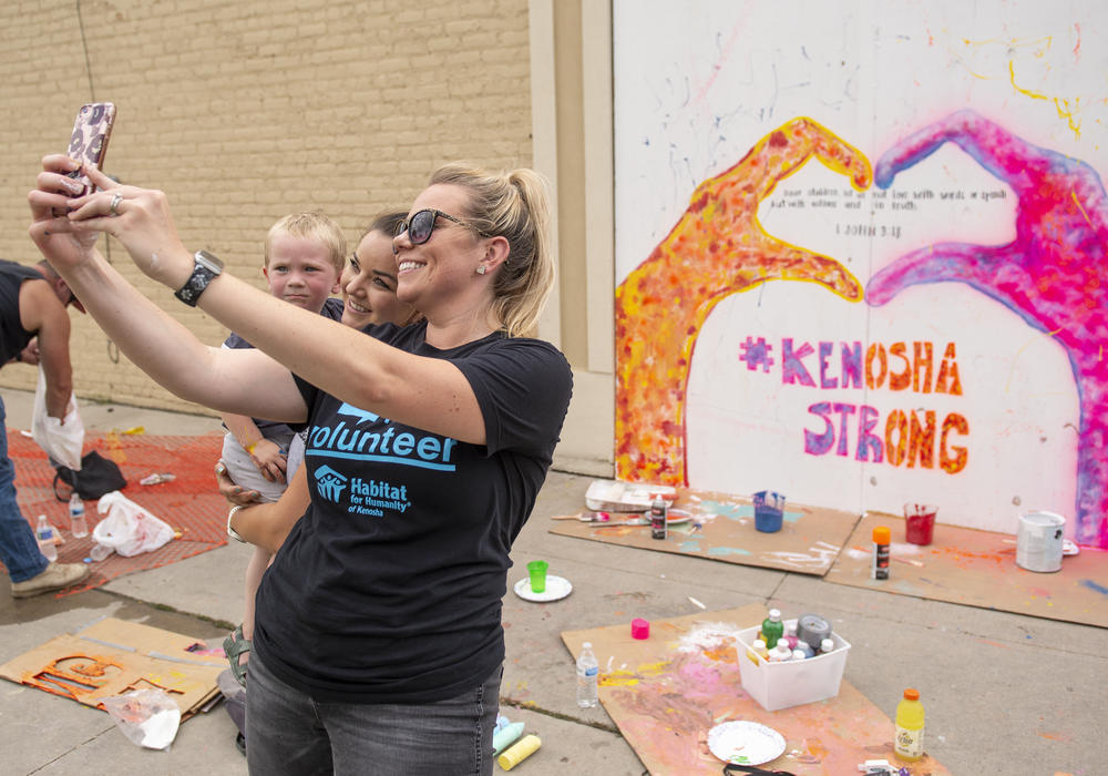 Angela Elliott (C) takes a picture in front of a mural she helped to create on the boarded windows of a business in the Uptown neighborhood of Kenosha, WI on August 28.