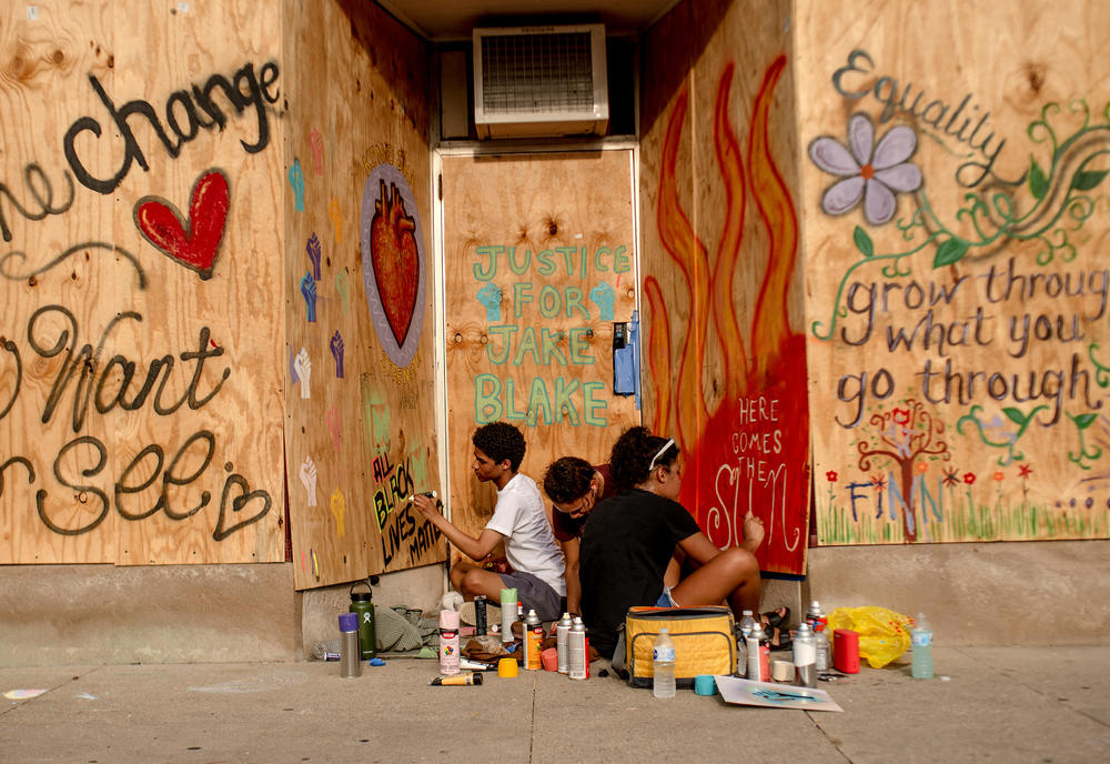 Kenteay Varnell, Mya Wilson, and Zipporah Gordon paint a mural on the boarded windows and door of a business.