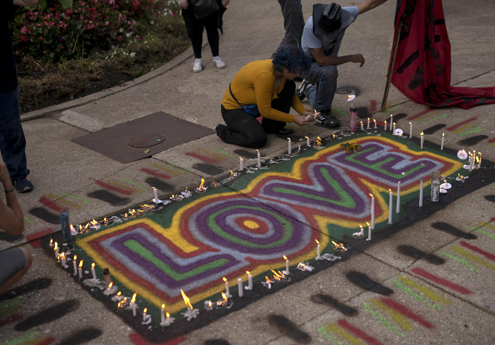 People place candles around an artwork that says 