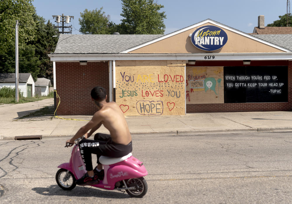 A man rides a scooter past a boarded-up Uptown Pantry in Kenosha, WI.