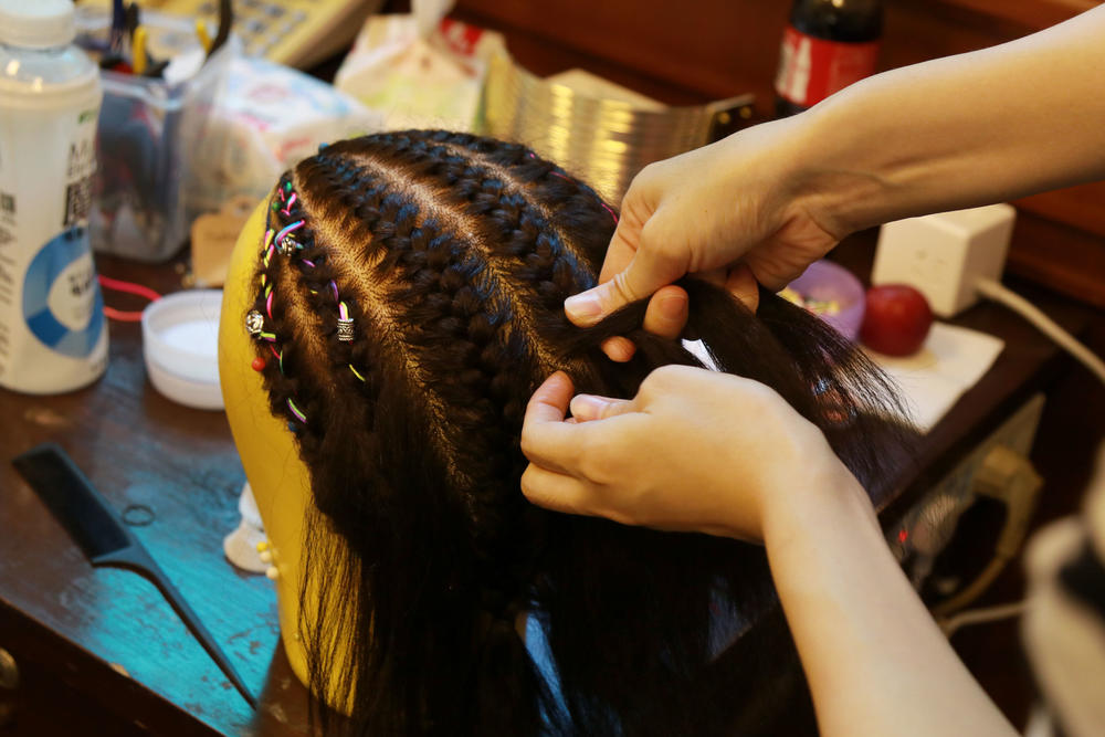 The production's costume designer braids a wig.