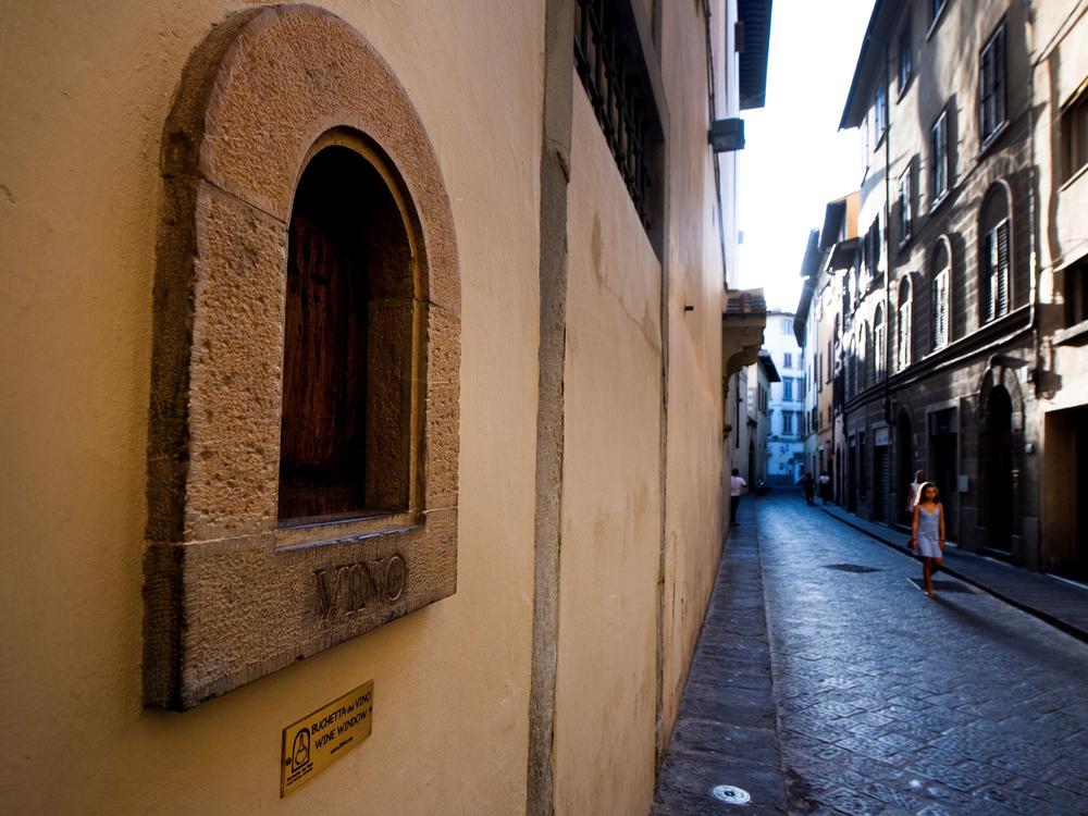 A girl walks past a <em>buchetta del vino</em>, a small window to serve wine, typical in Florence.