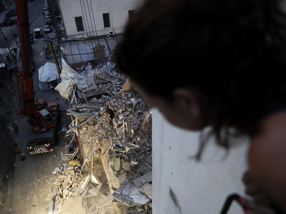 A woman watches from her apartment balcony as a crane removes the rubble of a building after a Chilean rescue team detected signals there may be a survivor at the site in Beirut, Lebanon, on Sept. 4, 2020.