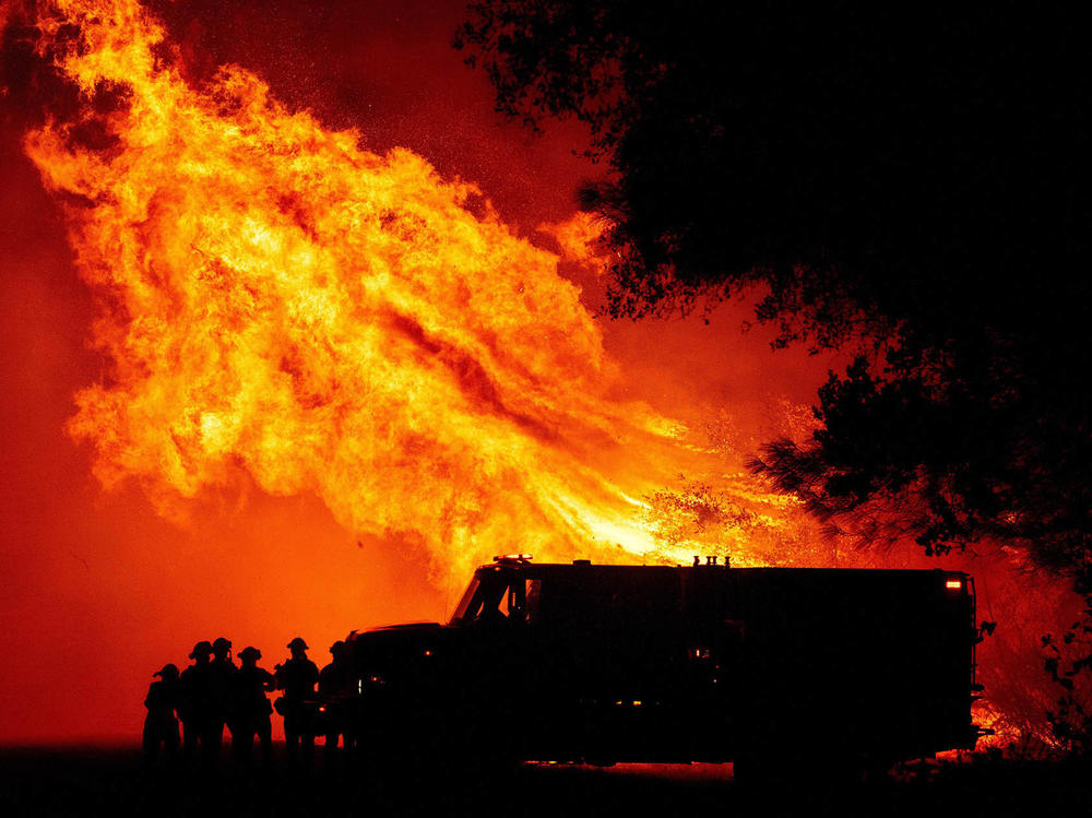 Communities have struggled to find funding to clear brush and make neighborhoods more safe from fires. Here, firefighters watch as flames tower over their truck in Oroville, Calif.